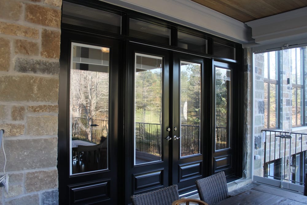 A black hinged garden door with sidelites and transoms, seen from a covered stone porch